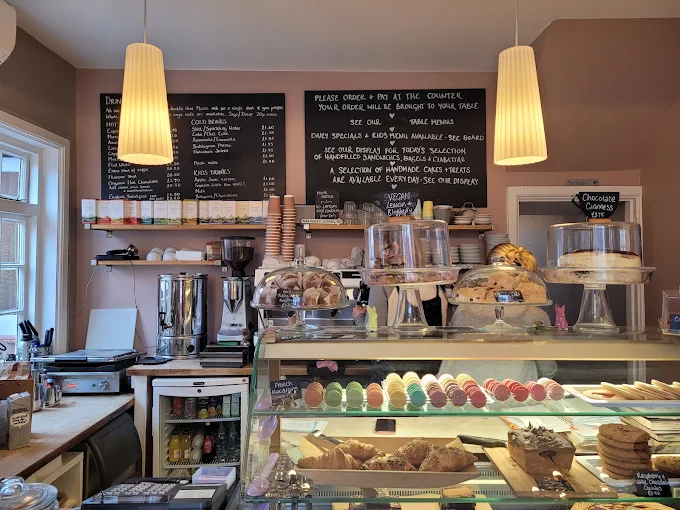 Interior of The Lavender House Cafe in Bromley showing the cake display counter, coffee machines and chalkboard menus under pendant lighting.